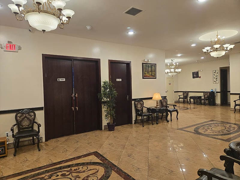 Interior hallway with seating area at Harmony Funeral Home in Brooklyn featuring chandeliers and comfortable waiting chairs.