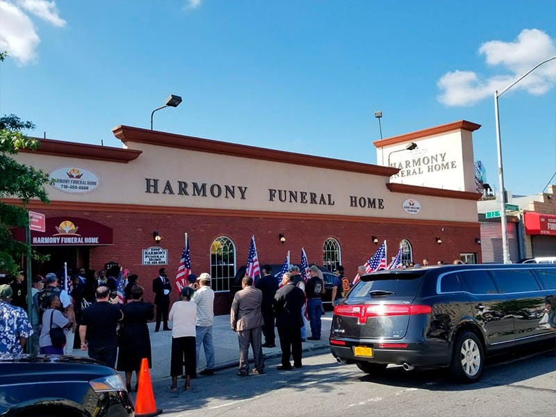 Memorial service gathering outside Harmony Funeral Home in Brooklyn with attendees and hearse present