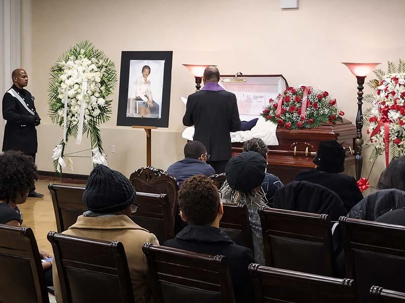 Traditional funeral service ceremony with minister speaking beside casket and floral arrangements in Brooklyn funeral home